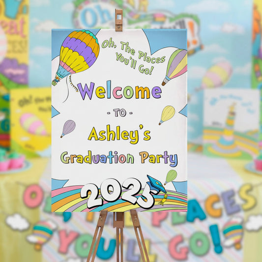 Graduation party sign with colorful balloons and text on a stand, surrounded by similar signs and decorations.